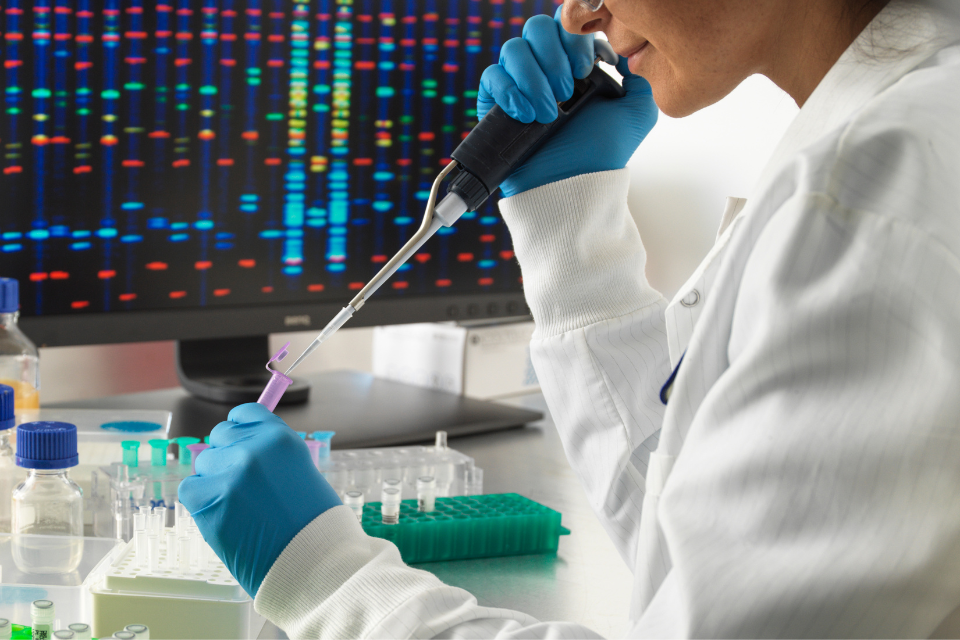 A scientist pipetting a sample in a lab, with a DNA sequencing display in the background, representing CFTR gene research on pancreatitis.