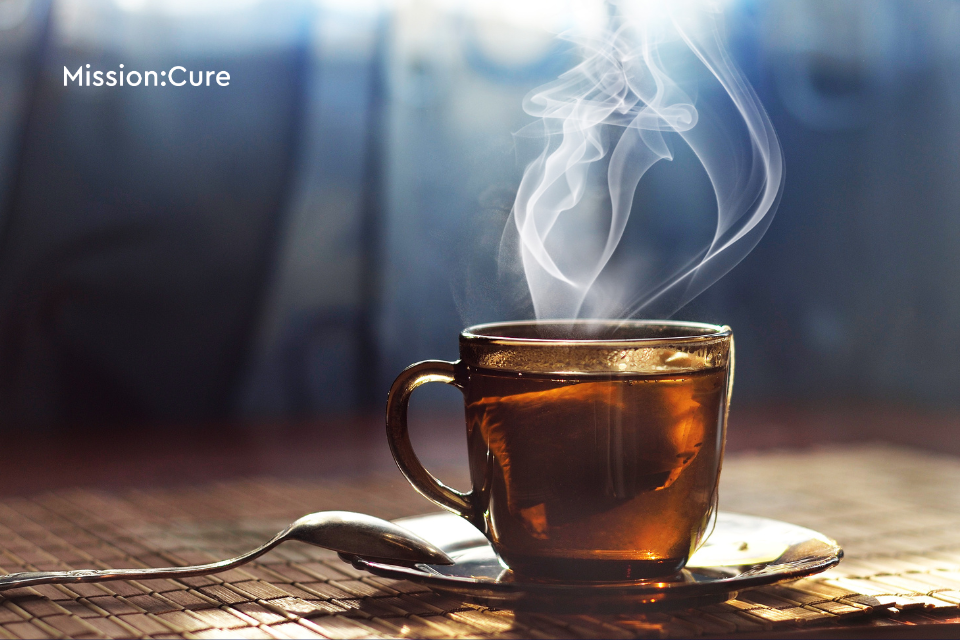 Steaming cup of tea in a brown cup. Mission: Cure logo in the top left corner.